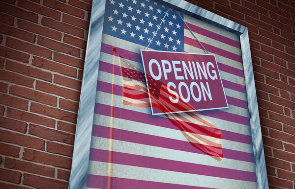 Poster on a brick wall featuring the American flag with a sign that reads ‘Opening Soon’ in bold white letters on a red background.