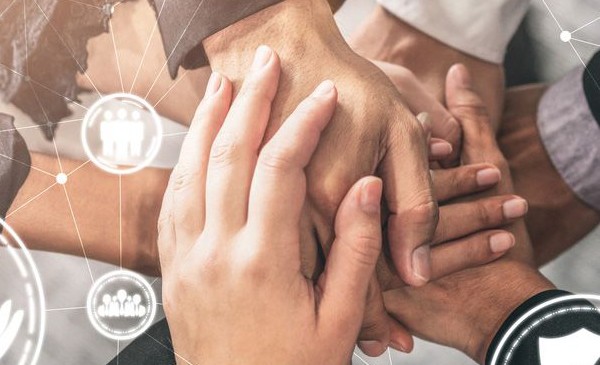 Close-up of multiple hands stacked together in a gesture of teamwork and unity, with abstract digital icons representing collaboration and connectivity overlaid on the image.