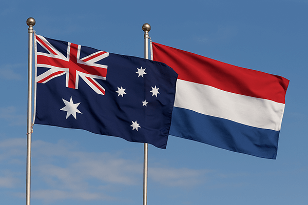 The Australian and Dutch national flags on flagpoles against a clear blue sky.
