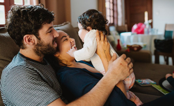 Brazilian father and mother playing with toddler on the sofa.