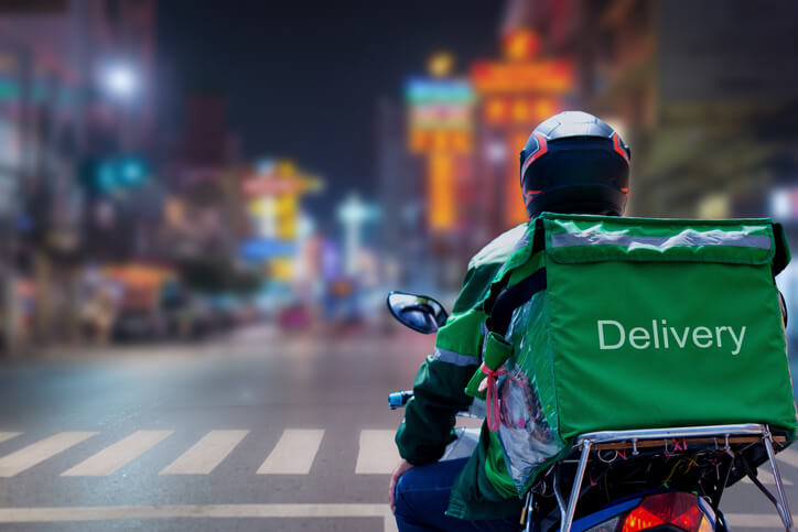 Food delivery driver on motorcycle at night on a busy, wet street.