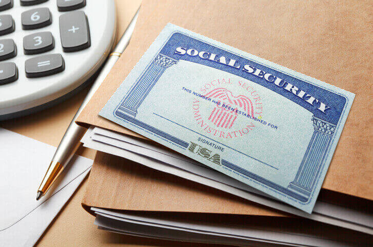 Social Security card on a brown folder, with a pen and calculator nearby.