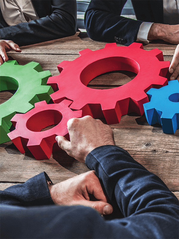 Businesspeople gathered around gears on a desk, symbolizing the interconnectedness of strategic workforce planning.