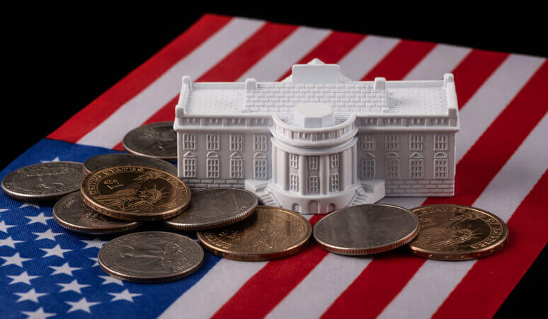 A miniature White House model sits on an American flag with coins scattered around it.